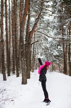 A girl in a pink scarf and hat stands in the middle of a pine forest. Beautiful pine forest on a frosty day