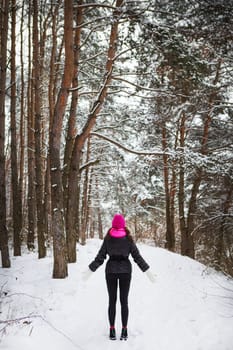 A girl in a pink scarf and hat stands in the middle of a pine forest. Beautiful pine forest on a frosty day