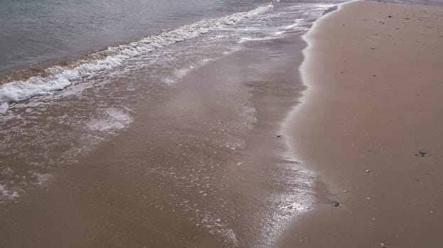 A secluded brown sand beach with gentle waves. Lines, sunny day, empty space ,