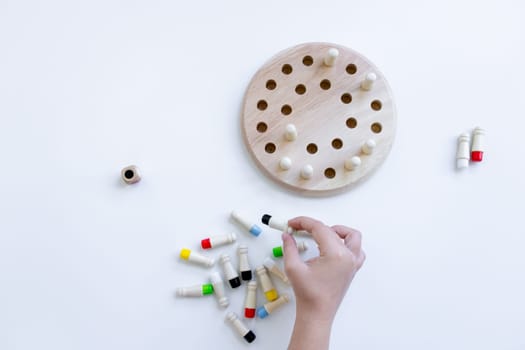 Hand playing strategy board game with wooden pegs and pegboard on white surface.