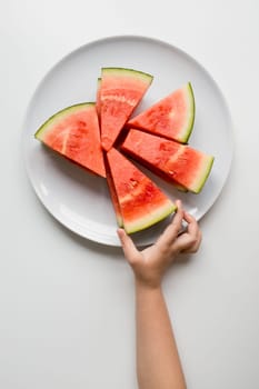Child hand reaching for fresh watermelon slices on a plate.