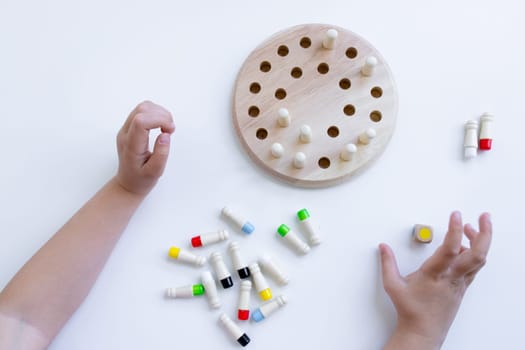 Child playing wooden memory game with colorful pegs and holes on white surface.