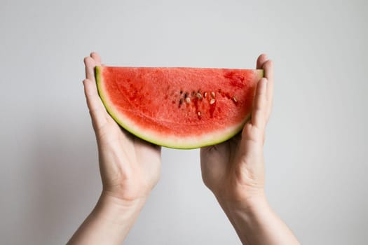 Hands holding fresh watermelon slice against white background.