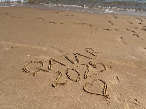 An inscription on a clean yellow sand beach in Doha, Qatar, 2025