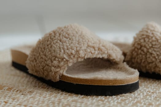 One beautiful home fashionable, stylish and warm slippers with natural coffee-colored sheepskin and cork sole stands on a jute rug on a white tiled floor in a room on a sunny day, bottom side view very close-up and depth of field. House shoes concept.