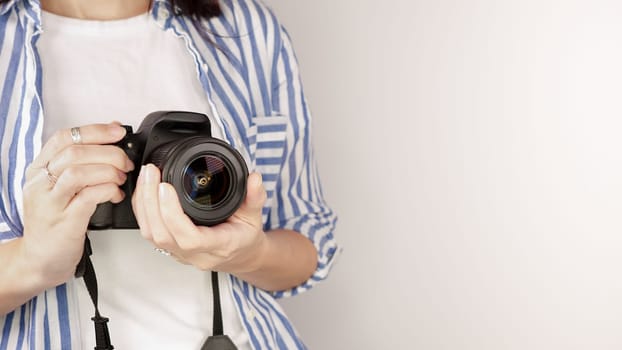 Photographer holding dslr camera. Self portrait, front view. Faceless nice woman with brown red hair in a tshirt with hands holding photo camera white background