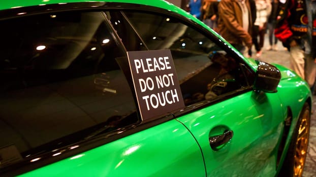 A prominent sign on a stunning green luxury sports car clearly states Please Do Not Touch. This eye-catching vehicle is a high-performance sports car designed for enthusiasts.