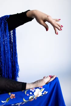 Asian female hand gesture with traditional blue embroidered shawl and red nails.