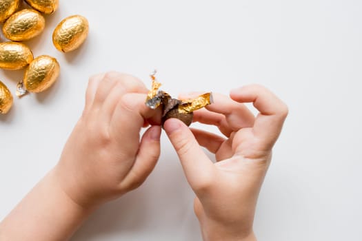 Childs hands unwrapping chocolate candy with golden foil wrapper.