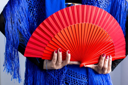 Female hands holding red fan with blue shawl in vibrant composition.