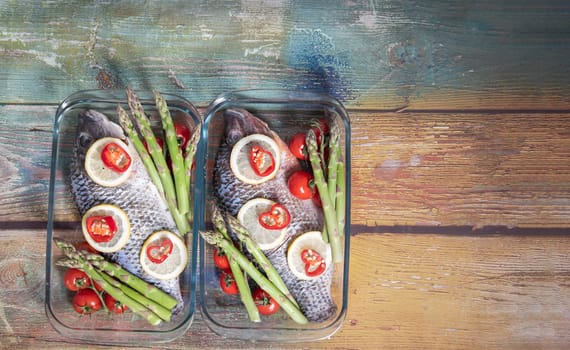 Raw green asparagus on fresh large dorado fish, tilapia, carp in a baking dish with cherry tomatoes,step by step recipe instructions, top view on an old wooden table
