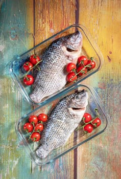 Fresh large dorado fish, tilapia, carp in baking dish with cherry tomatoes, step by step recipe instructions, top view on old green wooden table