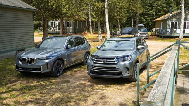 Ottawa, ON Canada - 07.07.2024: Two Parked Modern Compact Crossover SUVs BMW and Toyota in a Serene Wooded Area Surrounded by Lush Green Trees in camping area.