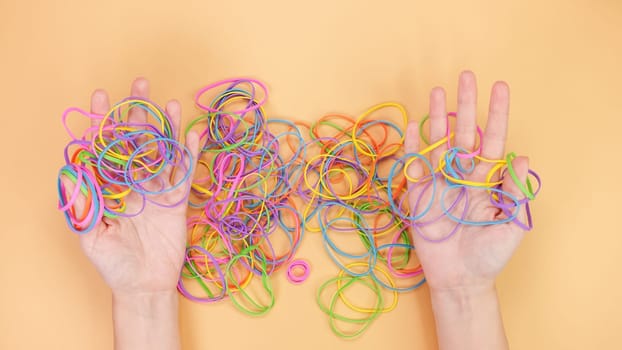 A collection of colorful rubber bands of various sizes tangles together on a soft peach background. The vibrant pink, blue, green, yellow, and orange hues create a playful and striking visual.