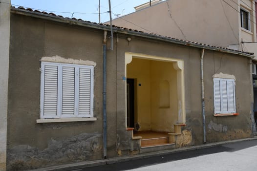 The house features a sunlit entrance framed by weathered walls and classic shutters, embodying a sense of tranquility on a serene street in a quaint neighborhood.