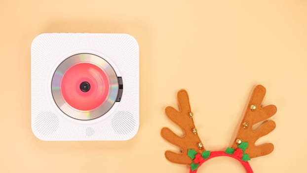 The image shows a white portable CD player with red headphones on a beige background. The CD player has a red light on the front, and the headphones are resting on the right side of the CD player.