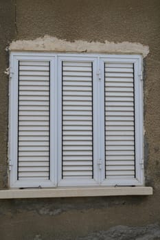 Three wooden shutters, slightly worn and painted white, adorn the exterior of a weathered building, reflecting the charm of a bygone era. The muted tones enhance its rustic allure.