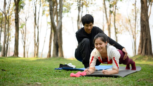 Man helping his partner during fitness exercise in a park. Healthy lifestyle concept.