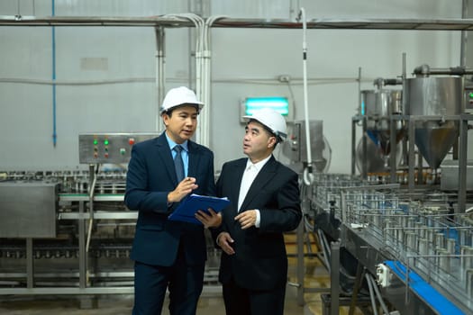 Factory supervisors in safety helmets examining a conveyor belt with metal cans in production plant.