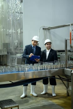 Factory supervisors in safety helmets examining a conveyor belt with metal cans in production plant.