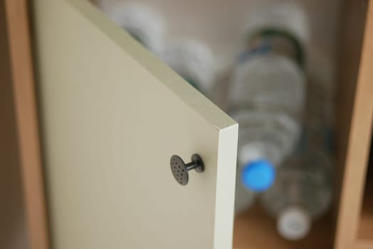 A kitchen cabinet door slightly open reveals water bottles inside.