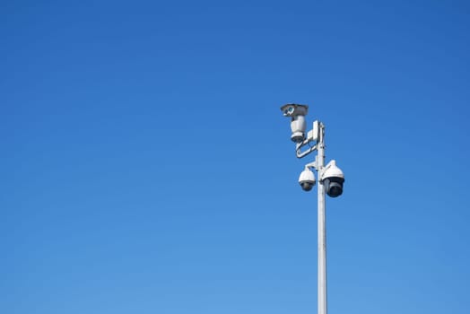 Surveillance cameras are installed on a tall pole under bright blue sky.