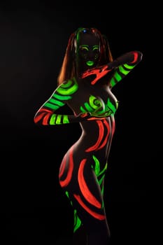 Full body of anonymous female with bright neon red and green fluorescent paints on naked body sitting on haunches in dark studio