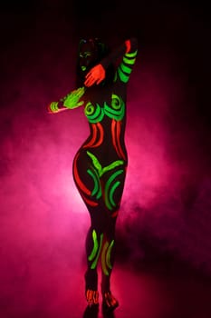 unrecognizable topless female model with bright UV paints on body and face dance in pink smoke
