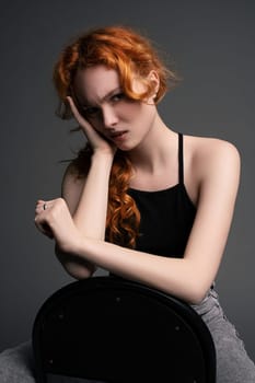 Cheerful redhead female model with ginger hair in casual outfits sitting on chair with sad emotion