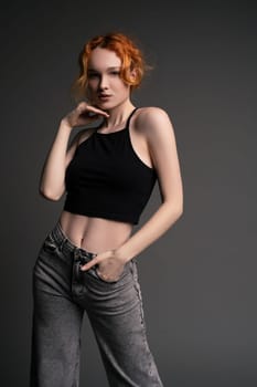 Portrait of young female model in trendy jeans and crop top with red hair touching head and looking at camera