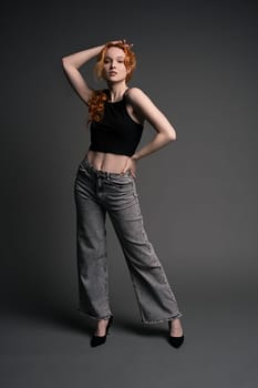 Full length of young female model in trendy jeans and crop top with red hair looking at camera during model test