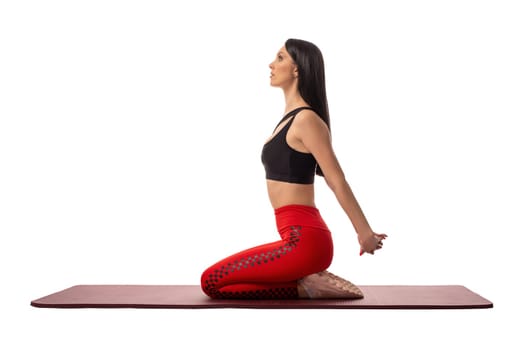 Side view of young slim female in sportswear sitting on mat and stretching legs while doing yoga in lotus pose against white background