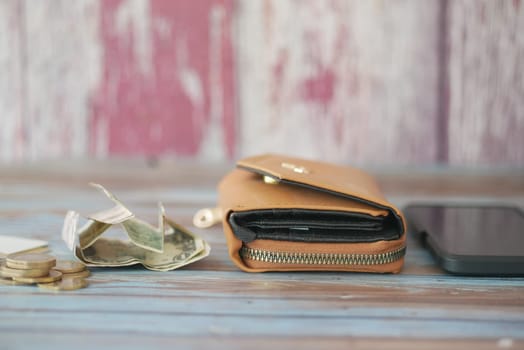 A brown wallet rests on a wooden table, surrounded by cash and coins.