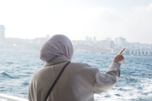 Woman in a light coat gestures toward the distant cityscape in Istanbul.