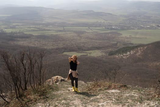 Person stands at hilltop edge, enjoying a vast valley view on a hazy day. Trees surround the foreground.
