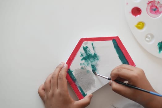 A young child paints a hexagonal canvas using vibrant colors and a brush.