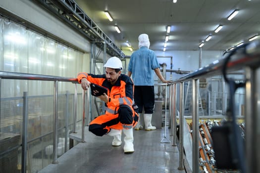 Factory engineer in protective uniform using digital tablet to inspect industrial equipment inside manufacturing facility.
