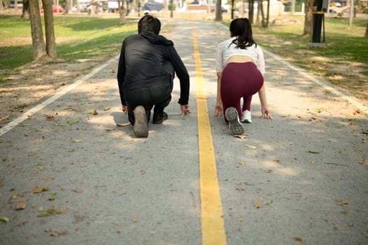 Young couple preparing to sprint in a park, crouched in starting position on a pathway.
