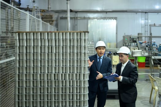 Two businessmen in hard hats discussing production plans inside a manufacturing facility.