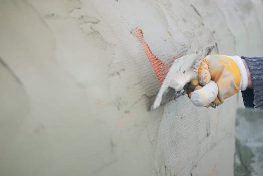 A construction worker smooths plaster on a wall using a trowel.