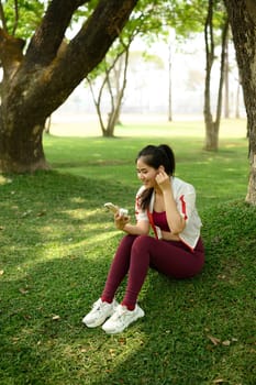 Smiling woman taking a break after workout using her smartphone with wireless earbuds.