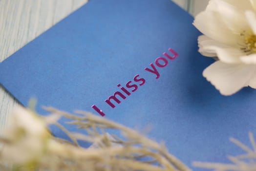 A blue card with the words I miss you surrounded by delicate flowers.