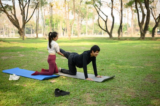 Young woman assisting partner with stretching in outdoor yoga session.