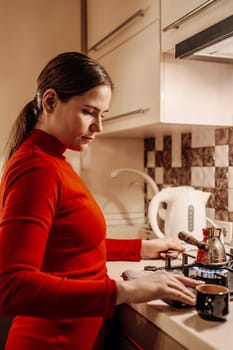 Woman in red long-sleeve shirt making coffee on a stovetop in her kitchen. A dark mug sits nearby.