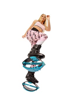 From below full body of young positive sportswoman with long blond hair in activewear jumping against white background in rebound shoes during workout