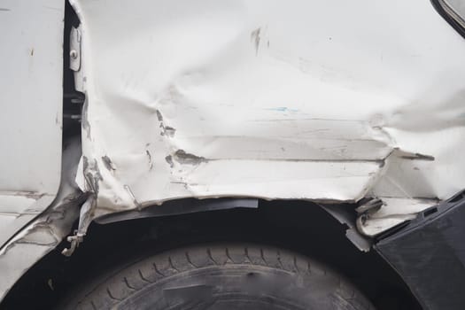 A white vehicle shows noticeable dents and scratches from a collision.