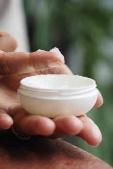 Hand applying petroleum jelly from white container in indoor setting.