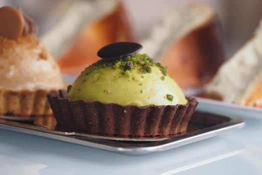 A vibrant green dessert sits elegantly on a tray, surrounded by pastries.