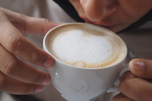 A person sips a foamy cup of coffee, savoring the moment indoors.