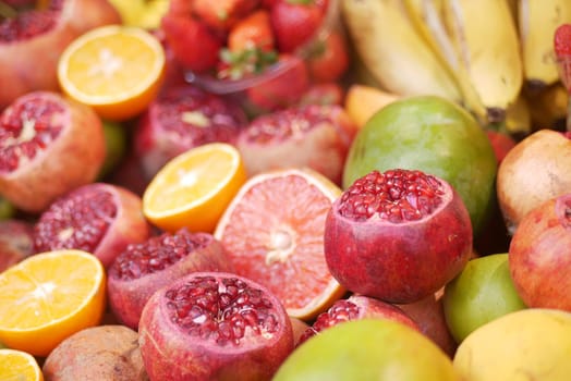 Vibrant assortment of pomegranates, oranges, and bananas at market.